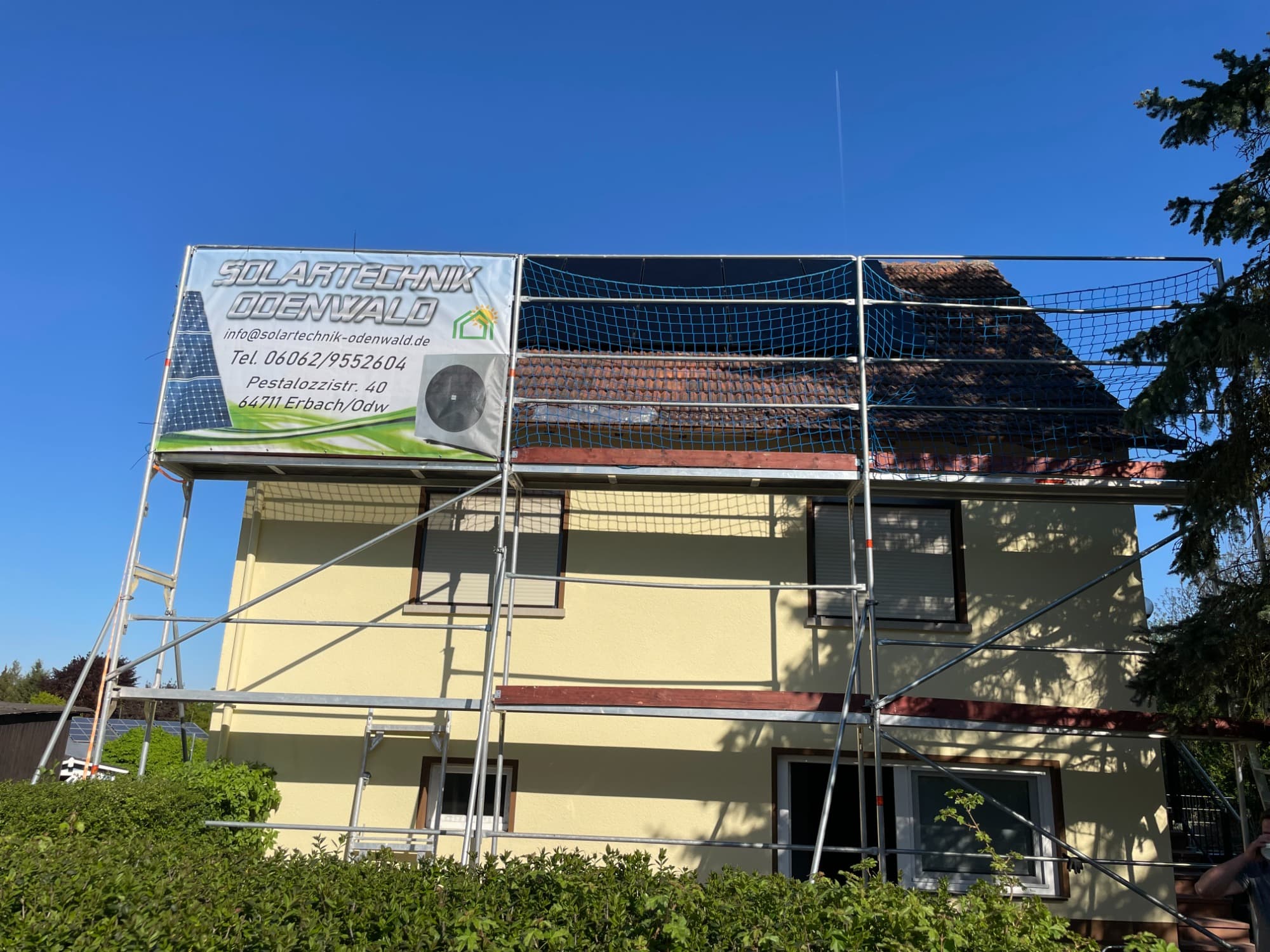 Gerüst mit Schutznetz an einem Wohnhaus, auf dem Steildach ein teilweise belegtes Modulfeld