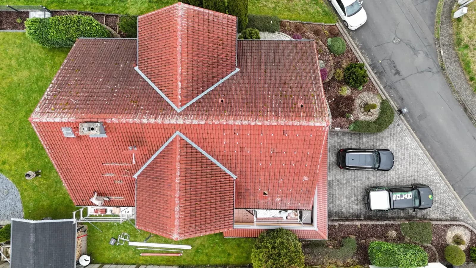 Senkrechte Drohnenaufnahme eines verwinkelten roten Ziegeldachs ohne Photovoltaik