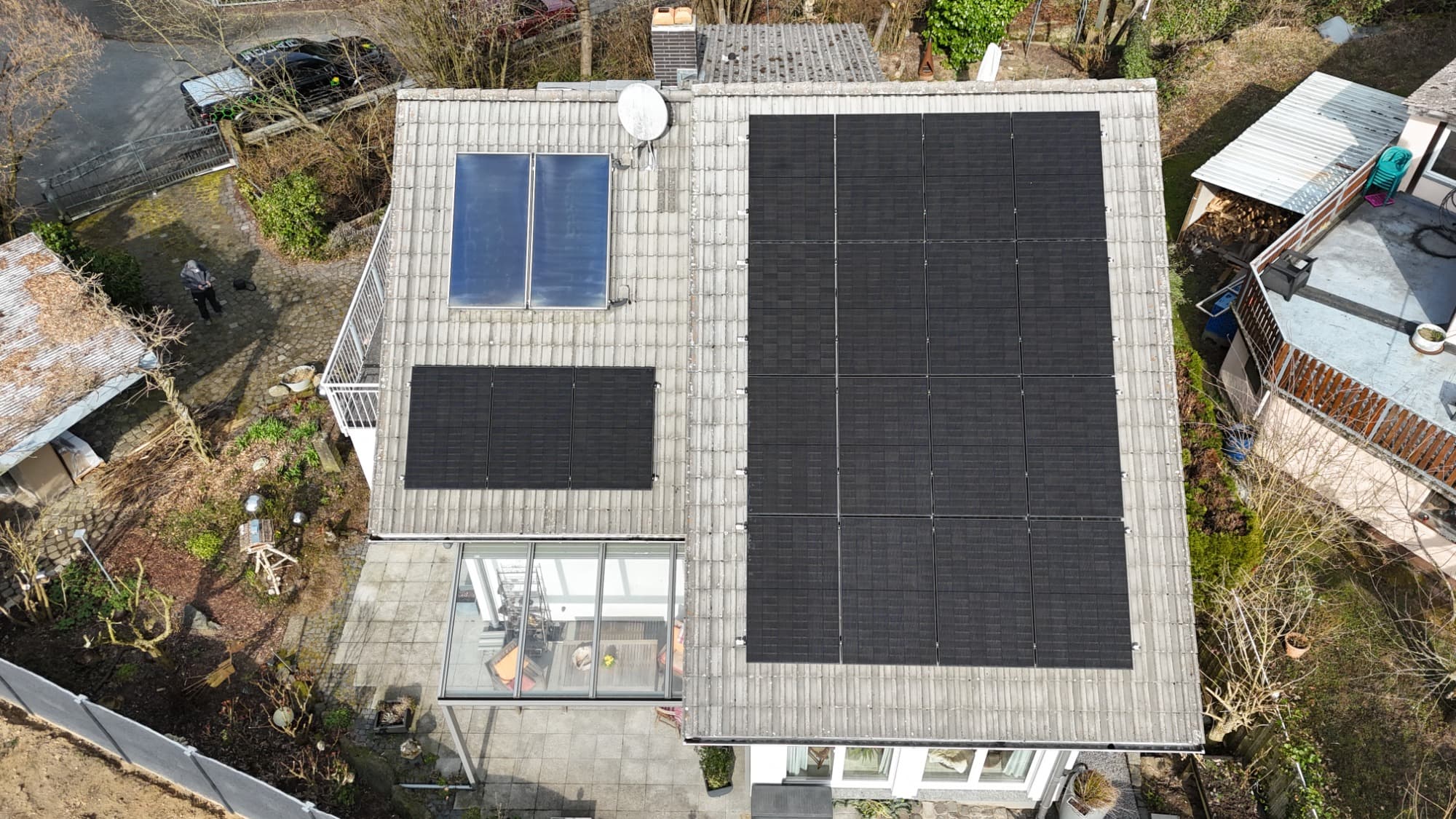 Senkrechte Drohnenaufnahme eines Wohnhauses: rechts ein geschlossenes Feld schwarzer PV-Module, links bleiben ältere Solarthermie-Kollektoren und die Satellitenschüssel ausgespart