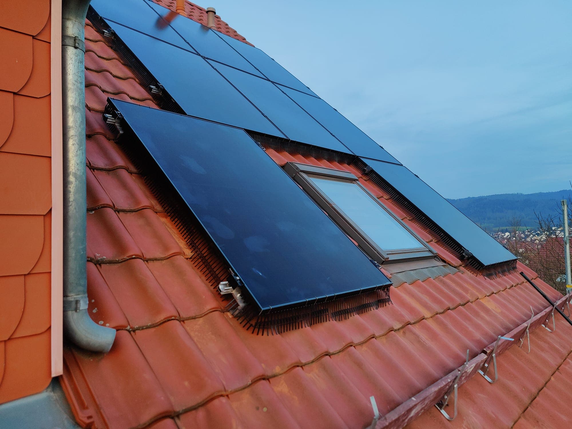 Solarmodule auf rotem Ziegeldach, rundum ein Bürstenband als Vogelschutz, daneben ein Dachflächenfenster