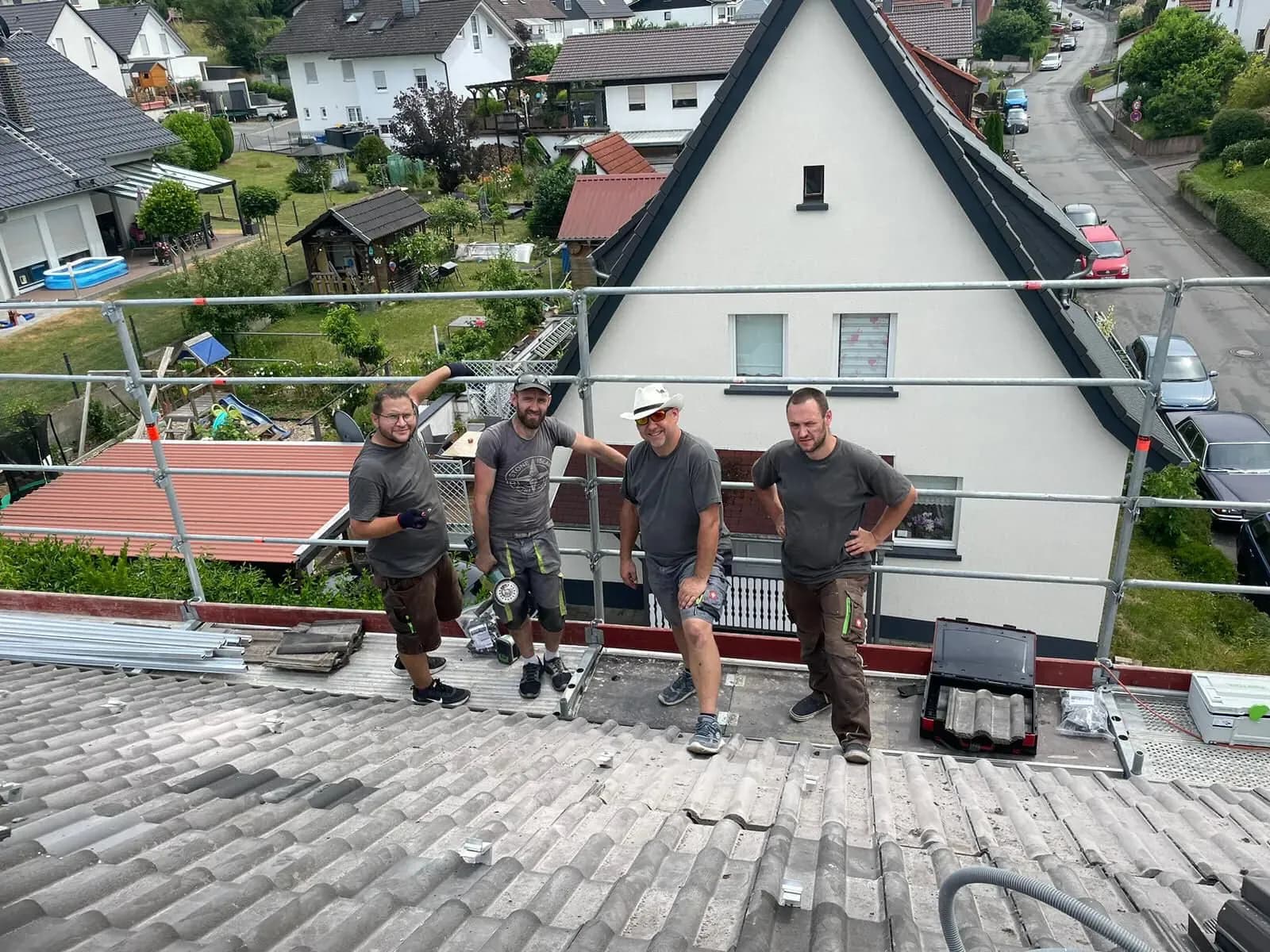 Vier Monteure stehen auf einem Steildach am Gerüst, die Dachhaken für die Unterkonstruktion sind gesetzt