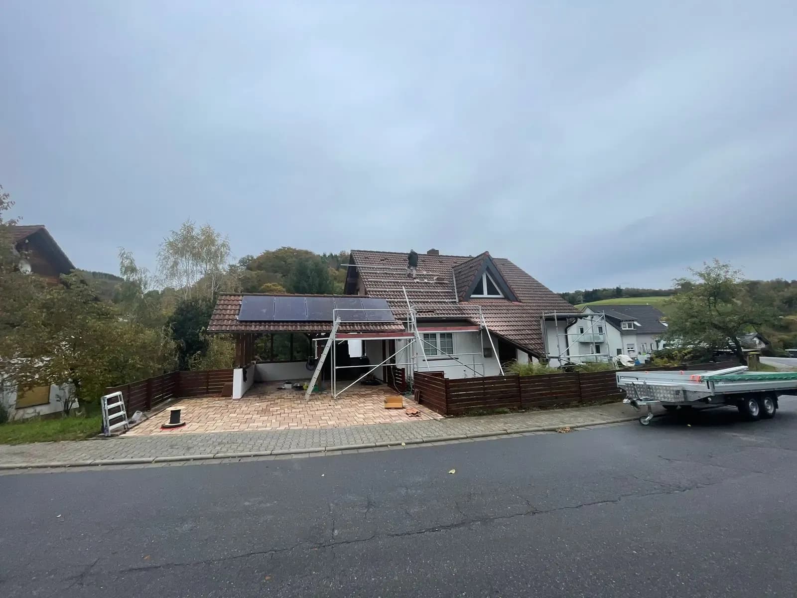 Wohnhaus im Herbst mit Gerüst am Giebel, auf dem Terrassenvordach liegen bereits Module