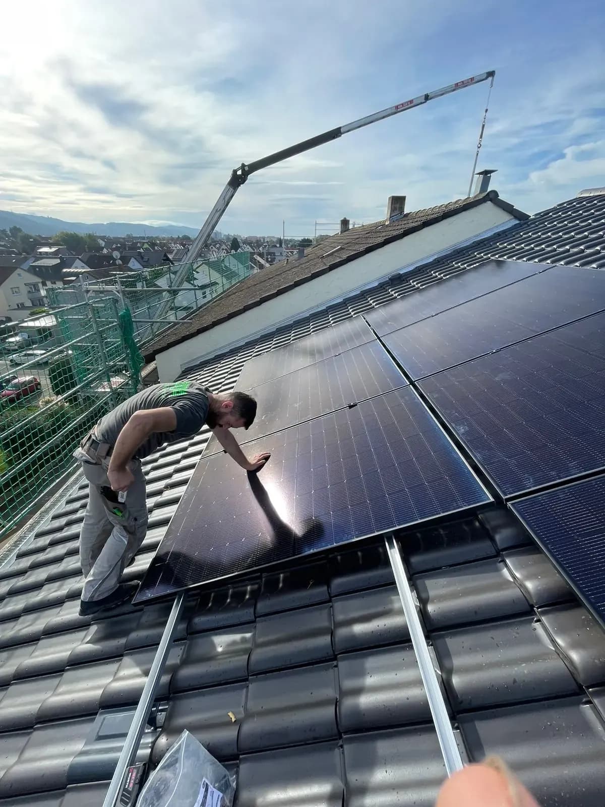 Monteur legt ein Solarmodul in die Trageschienen ein, im Hintergrund der Ausleger eines Krans