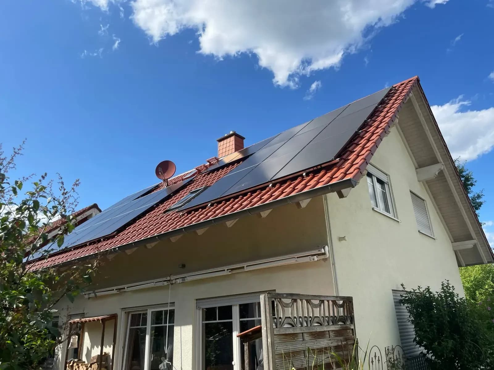 Sonnenbeschienenes rotes Ziegeldach mit schwarzen Modulen beidseits des Kamins