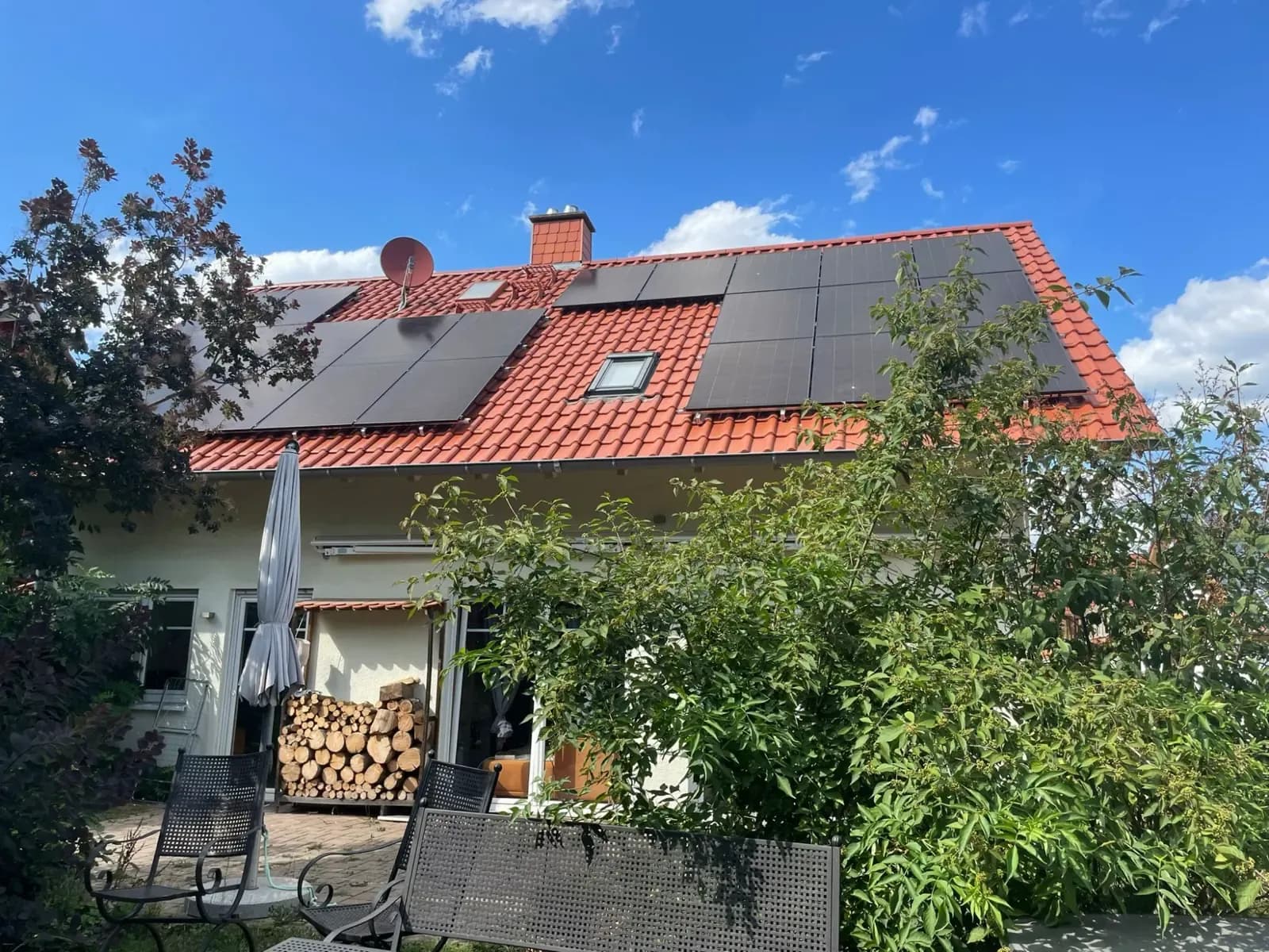 Fertige Photovoltaikanlage auf rotem Ziegeldach, die Modulfelder sind um Dachfenster, Kamin und Satellitenschüssel geplant