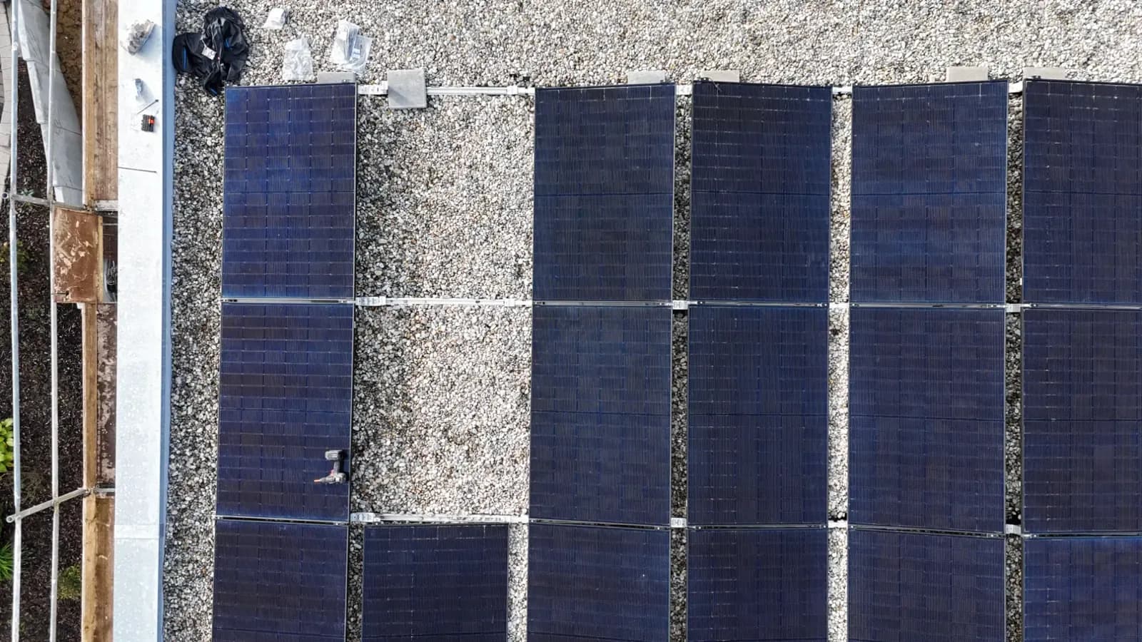 Detailaufnahme von oben: Solarmodule liegen in Reihen auf der Kiesfläche eines Flachdachs