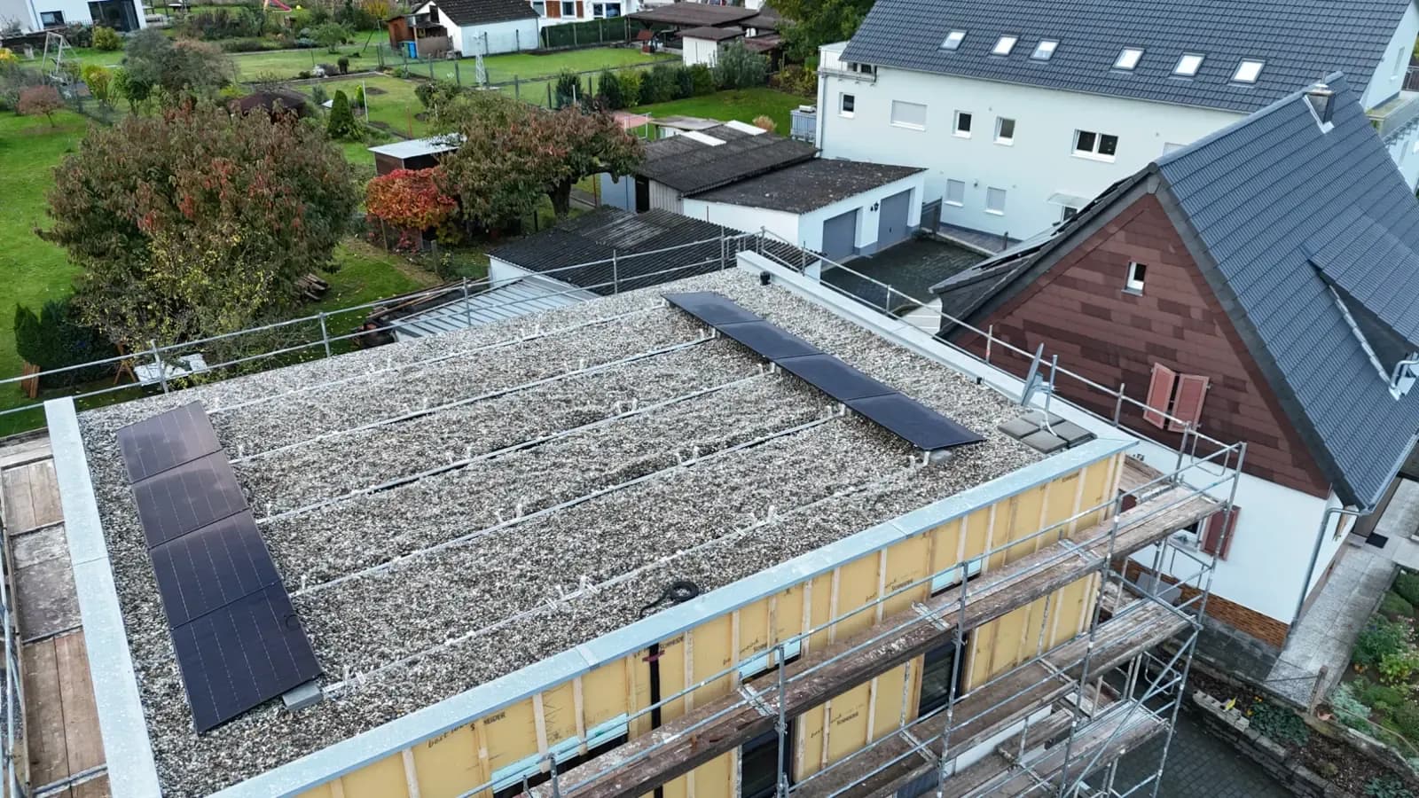 Kiesflachdach mit montiertem Trägersystem und ersten aufgelegten Modulreihen, ringsum ein Gerüst