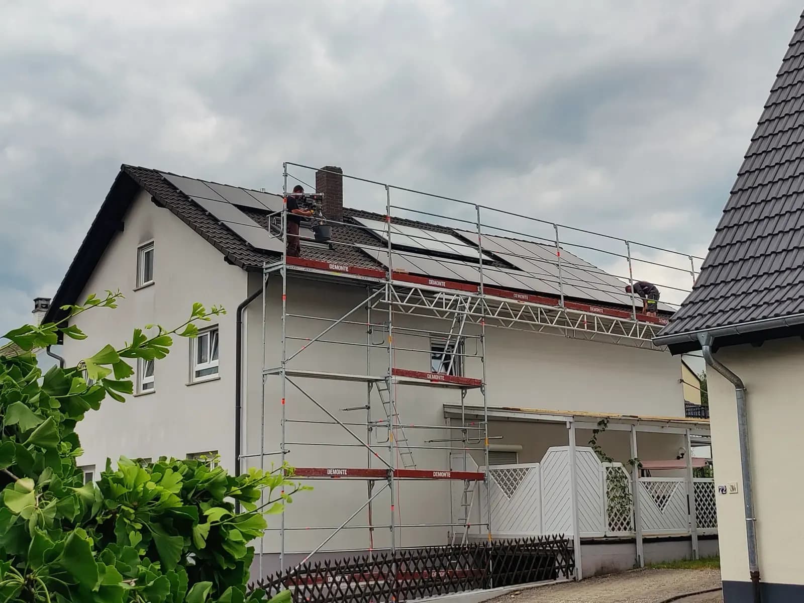 Zwei Monteure auf einem Satteldach, davor ein Gerüst über die gesamte Traufseite