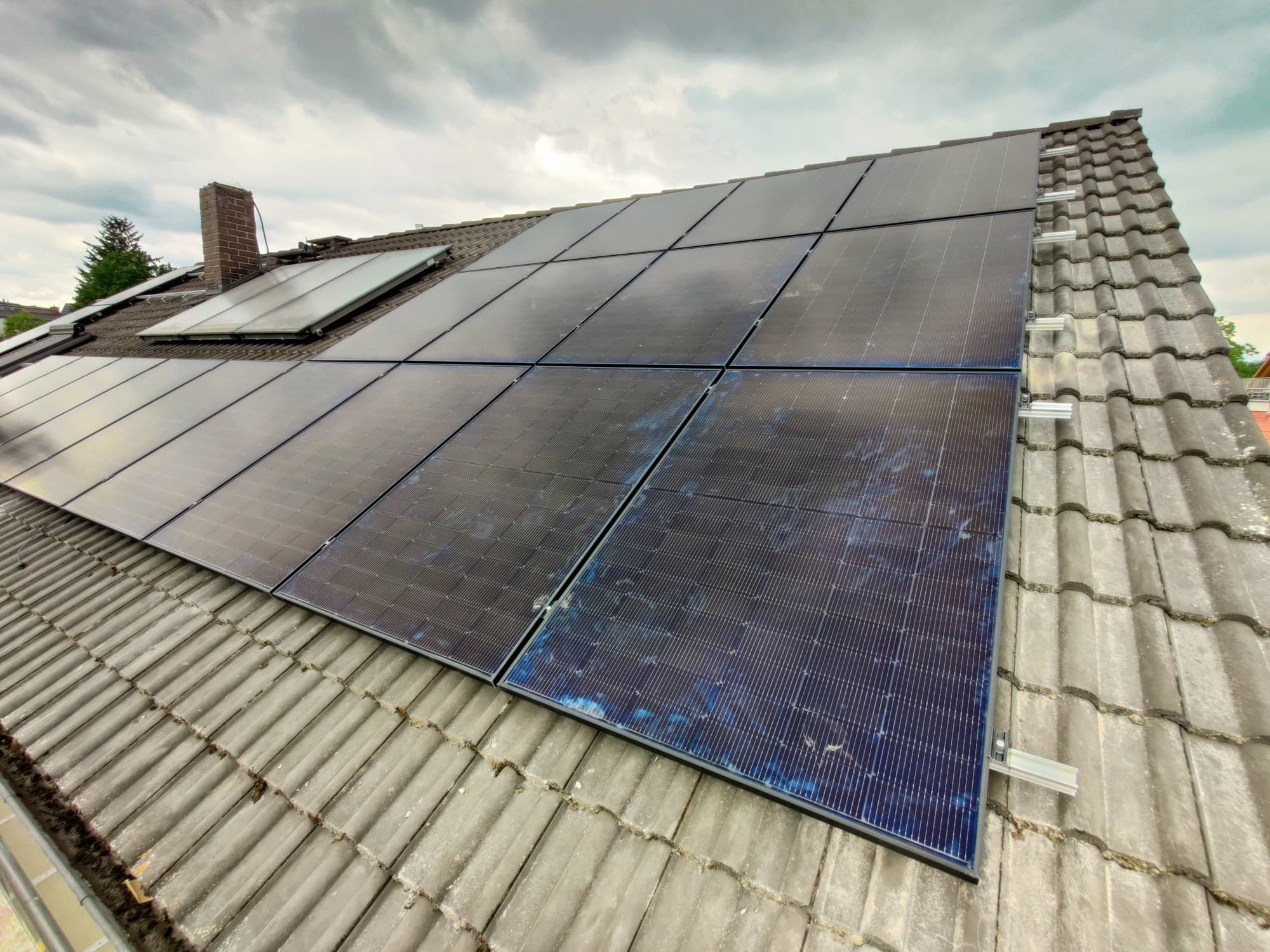 Fertig montiertes Photovoltaik-Modulfeld auf einem grauen Ziegeldach neben einem Dachflächenfenster