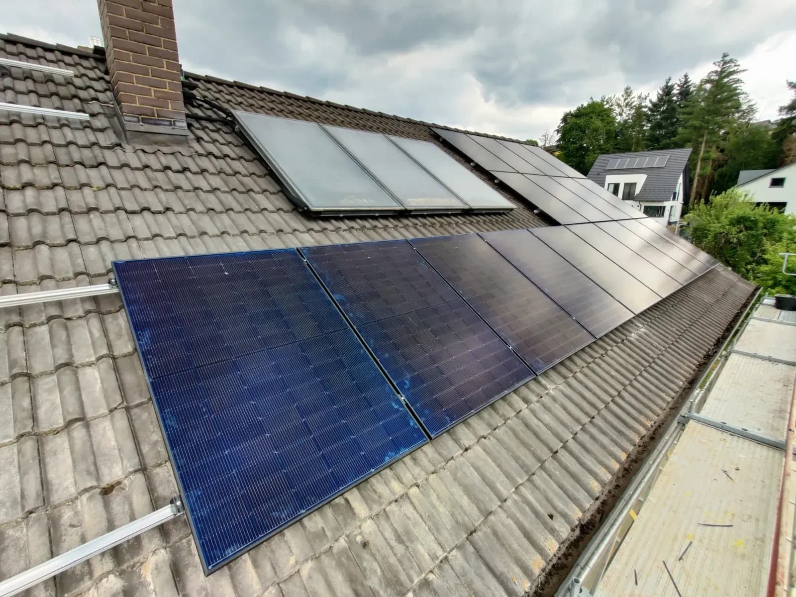 Modulfeld auf grauem Ziegeldach neben einer Reihe von Dachflächenfenstern und einem Kamin
